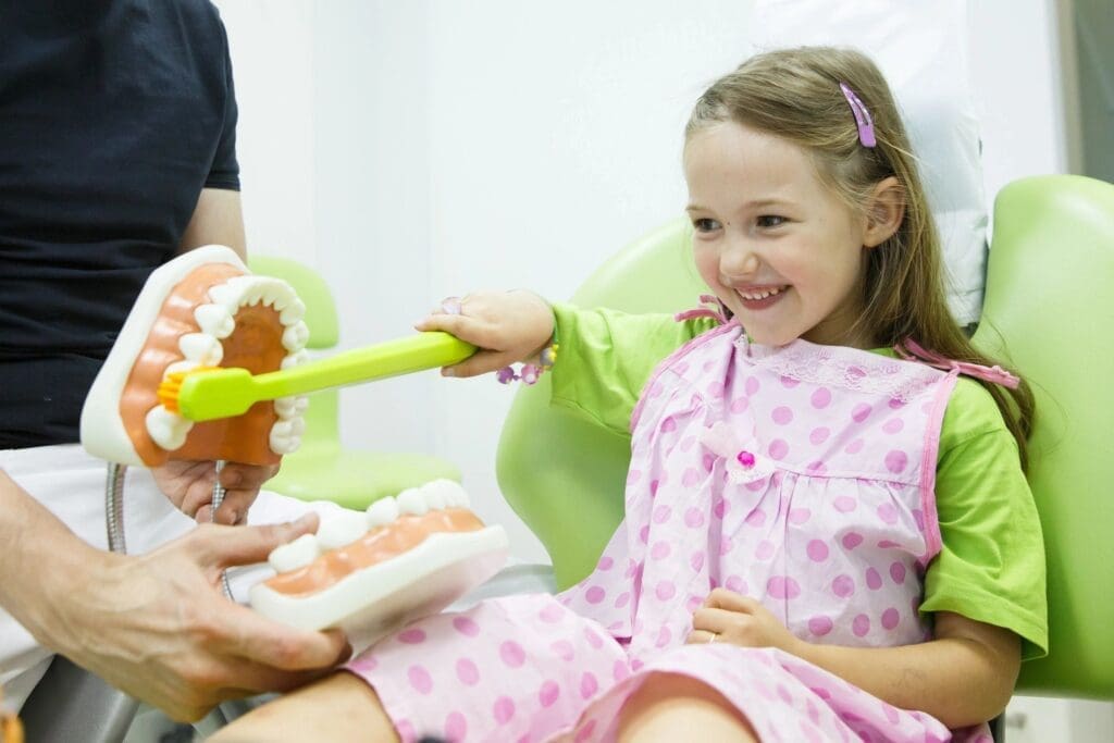 A little girl in pink pajamas brushing her teeth.