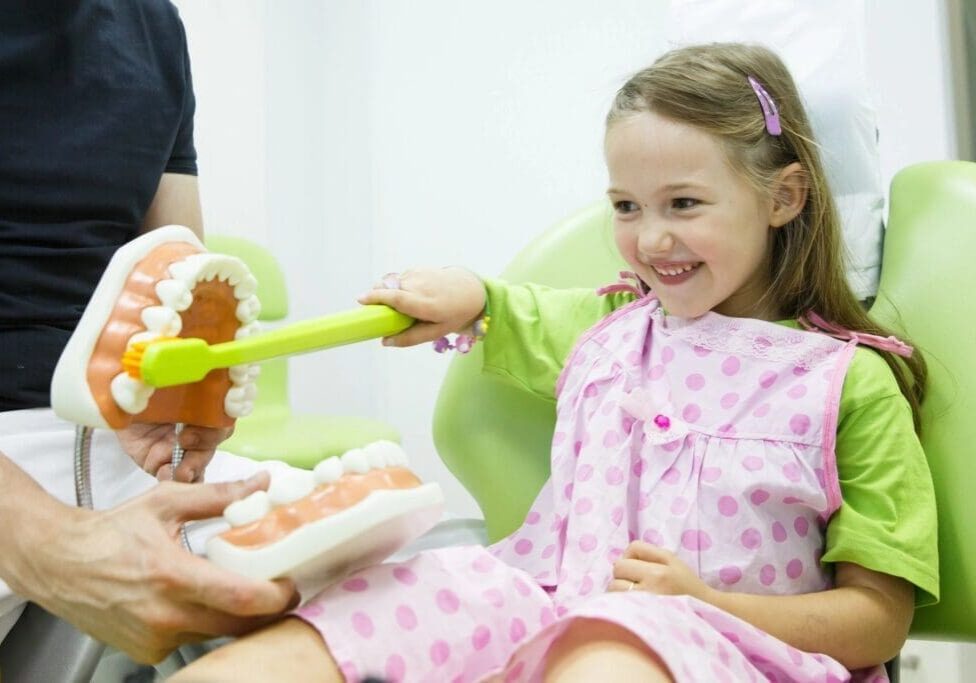 A little girl in pink pajamas brushing her teeth.